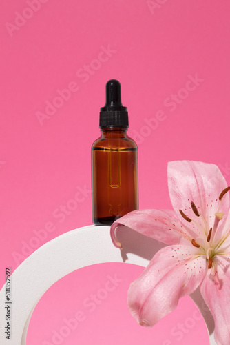 Cosmetic glass bottle with dropper for essential oils and serum on a podium with lily flower. Face and body care spa concept and natural cosmetics