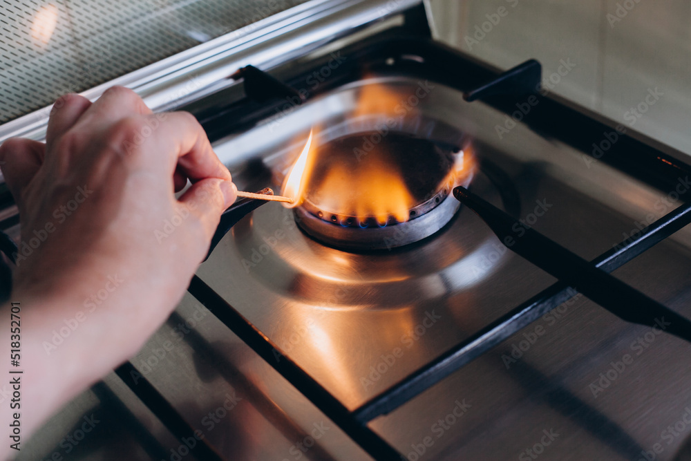A woman's hand with matchstick lights gas stove in her apartment