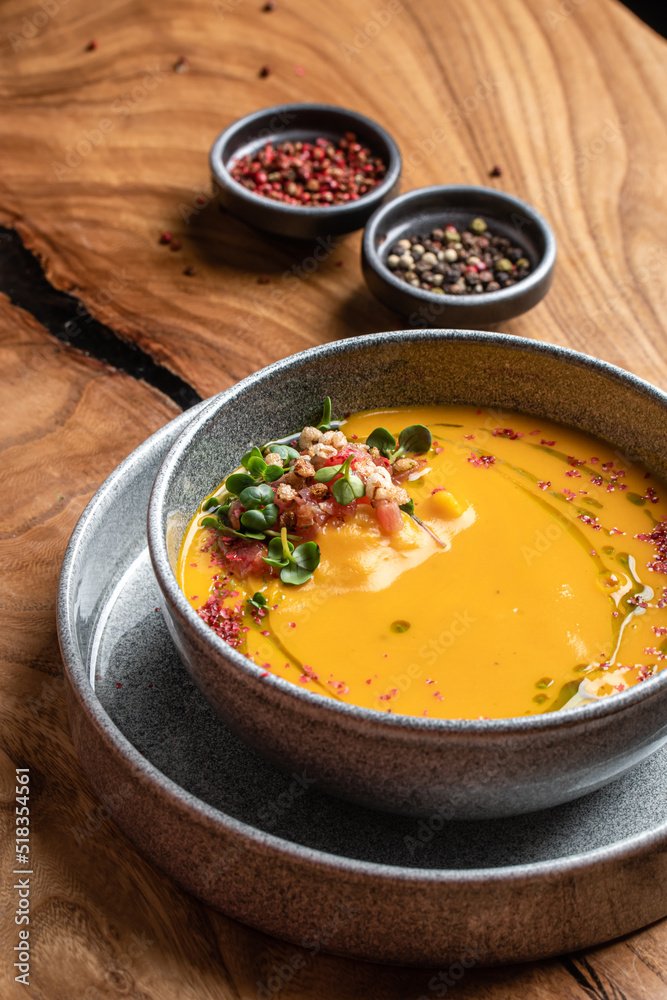 A bowl of pumpkin cream soup garnished with microgreens and tomatoes served in a gray bowl. restaurant food