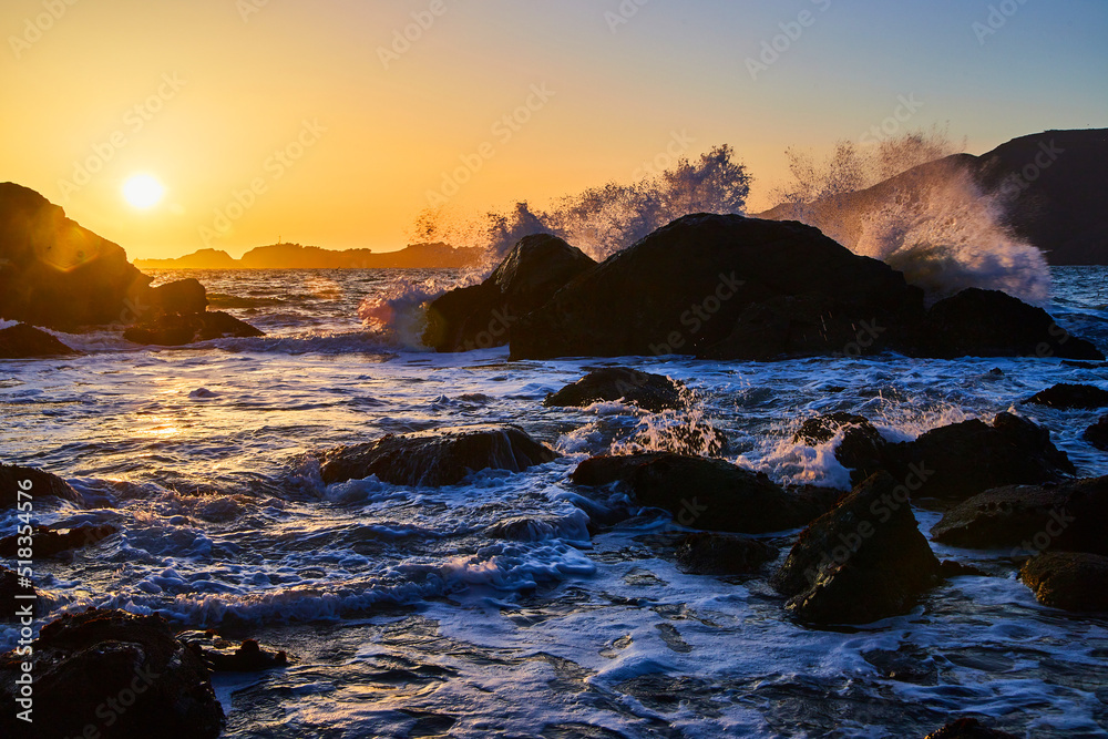 Waves crashing over boulders on ocean during sunset