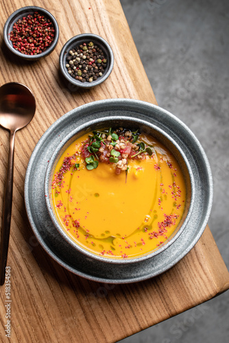 A plate of pumpkin cream soup garnished with microgreens and tomatoes on a wooden table, top view. restaurant food