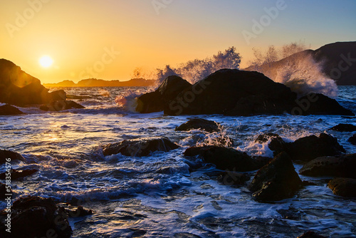 Waves crashing over boulders on ocean during sunset
