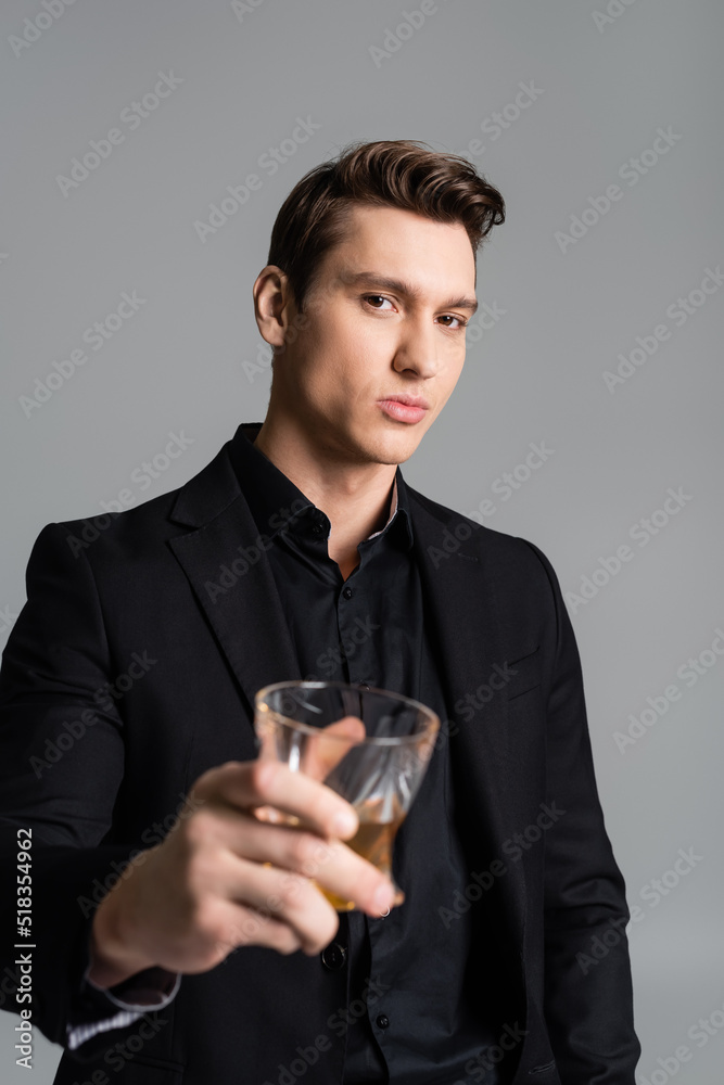 confident man in formal wear toasting with blurred glass of whiskey isolated on grey. confident man in formal wear toasting with blurred glass of whiskey isolated on grey.