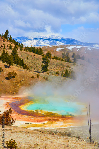 View of steamy hot spring from above overlooking snowy mountains by Yellowstone