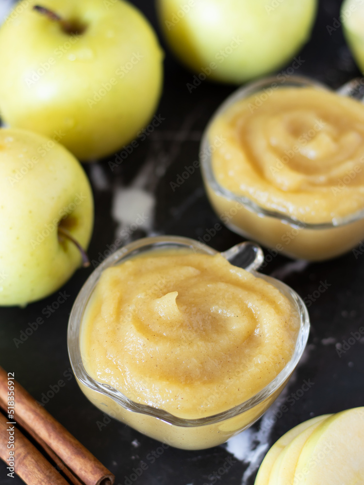 Organic homemade apple puree with a swirl on top in a glass bowl with cinnamon and golden delicious apple on a dark background. Healthy blended baby food, natural applesauce in a dish. Vertical shot.