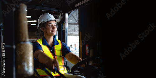 A female factory worker is driving a forklift in a large warehouse. A caring female factory worker drives a forklift in the factory. Transportation, transportation, logistics. © KANGWANS