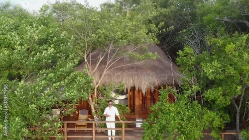 Aerial shot flying away from a young man drinking and celebrating life in a bungalow house with oceanfront view