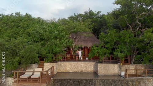 Aerial shot flying away from a young couple drinking and celebrating life in a bungalow house with oceanfront view