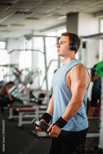 handsome young man and big muscles in sportswear. A young man holds dumbbells while exercising in the gym. Healthy sport lifestyle, fitness concept.