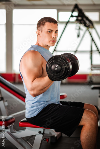 Muscular man trains in the gym, doing exercises with dumbbells for biceps, strong male abs