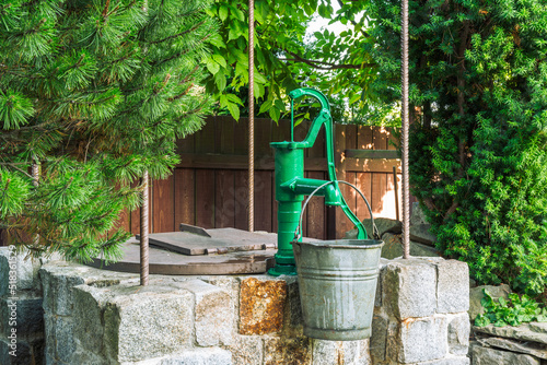 Bild auf Leinwand Stone water well with an old metal bucket in green garden