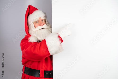 Santa Claus peeks out from behind an ad on a white background. Merry Christmas.