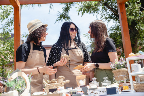 Valokuva Three brunette women sellers of European appearance in aprons at a street fair l