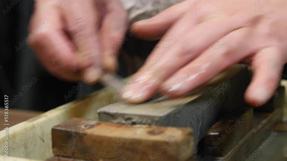 Master swordsmith is sharpening knife on grindstone with water
