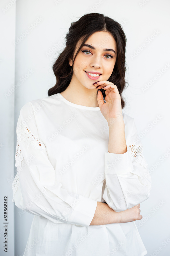 Beauty front portrait of a beautiful smiling young woman wear white shirt, posing in a studio holding hand near face, isolated white background. Beauty front portrait of a beautiful smiling young woman wear white shirt, posing in a studio holding hand near face, isolated white background.