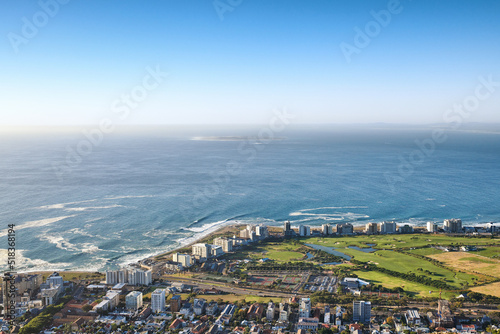 Landscape view of a beautiful coastal city near the beach on a summer day. Aerial view of a popular tourist urban town with greenery and nature during summer. Top view ocean and residential buildings