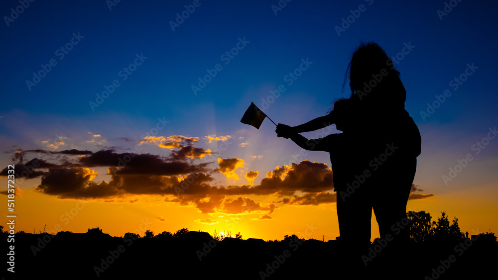 Ukrainian victory concept, silhouette of a mother with a child holding a flag against a yellow-blue sky.