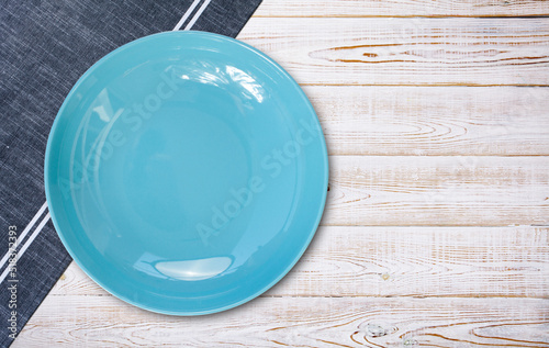 Empty blue plate and tablecloth on wooden desk, flat lay