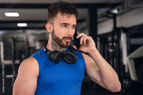 Handsome male with tattoos in his 20s talking on the phone in the gym