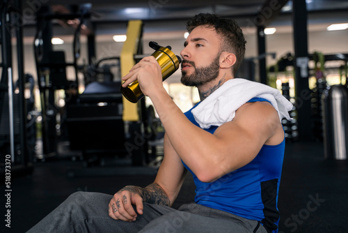 Handsome male with tattoos in his 20s drinking water in the gym