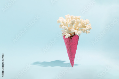 Pinck Ice cream cone with coral against pastel blue background. Minimal summer creative concept. Unusual ice cream.