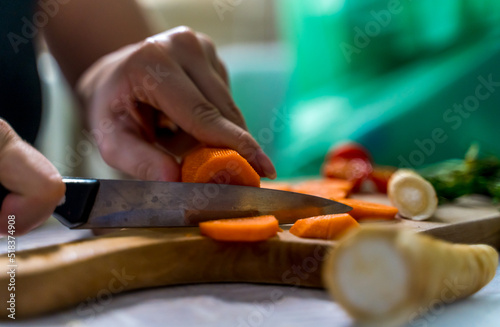 A girl is cutting carrot and vegetables on a wooden cutting board during the day