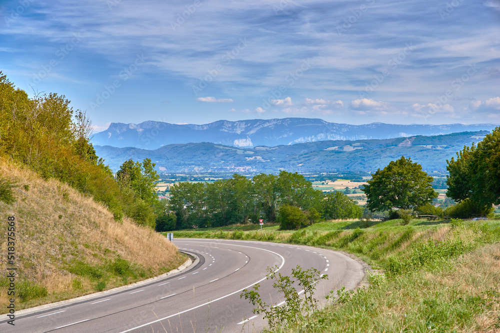 Scenic countryside route on a sunny day in Summer. Empty curved road with a beautiful view of nature, and a background landscape of the farmlands, mountains and cloudy blue sky.