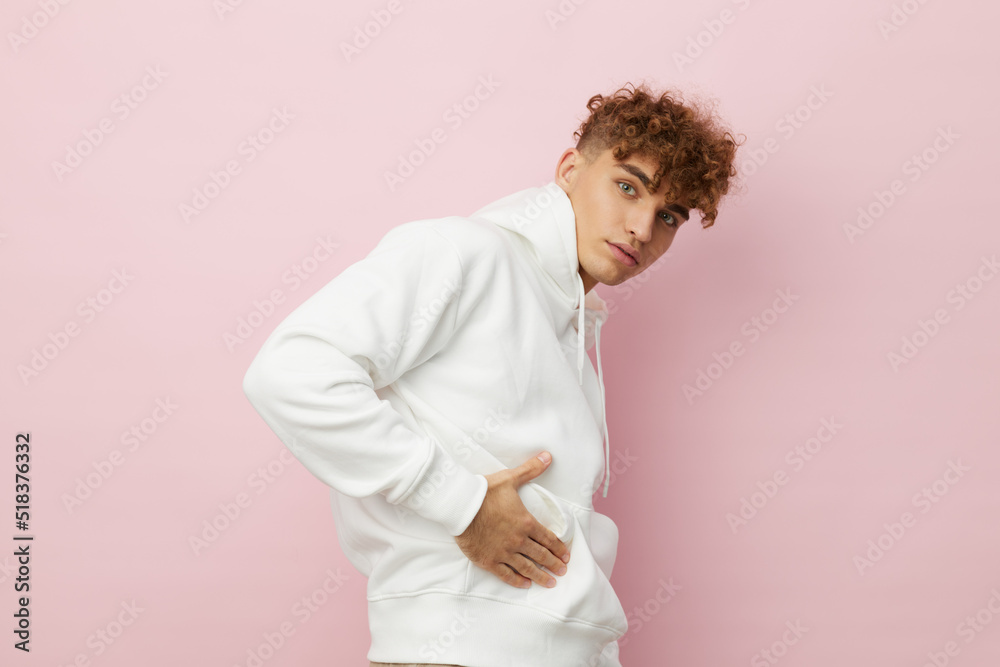 a handsome, attractive man stands on a pink background in a stylish white hoodie with his hands in his pockets. Horizontal Studio Photography