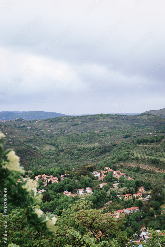Top view of a European village in the green hills. Italian houses with red roofs, orchards in the valleys, and rich greenery.