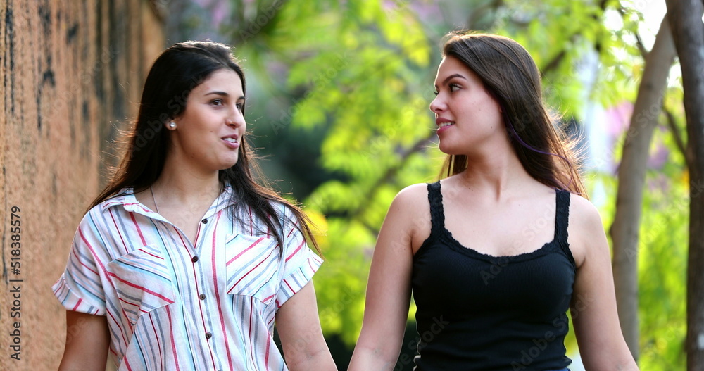 Girlfriends walking outside in sidewalk chatting in conversation Girlfriends walking outside in sidewalk chatting in conversation