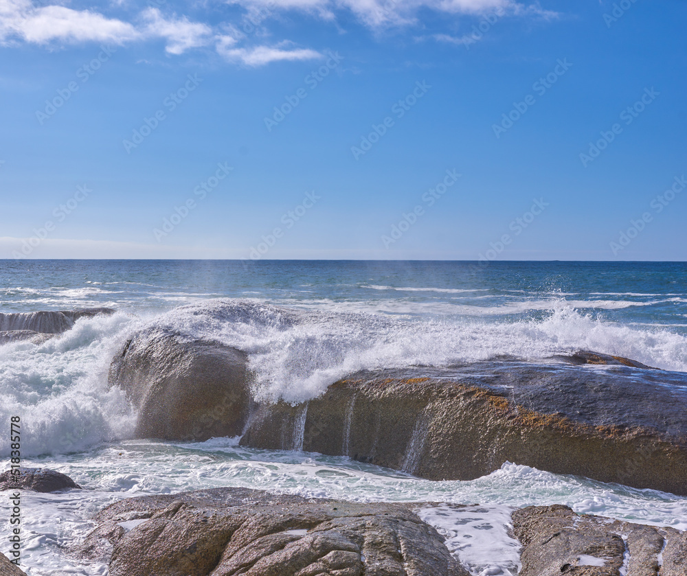 Rocks in the ocean under a cloudy blue sky with copy space. Scenic landscape of beach waves splashing against boulders or big stones in the sea at a popular summer location in Cape Town, South Africa Rocks in the ocean under a cloudy blue sky with copy space. Scenic landscape of beach waves splashing against boulders or big stones in the sea at a popular summer location in Cape Town, South Africa