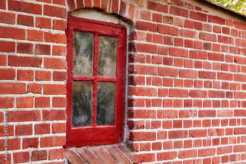 Old dirty window in a red brick house or home. Ancient casement with red wood frame on a historic building with clumpy paint texture. Exterior details of a windowsill in a traditional town or village photo