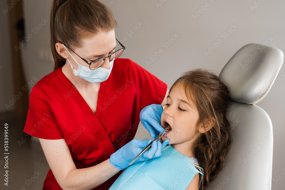 Pediatric dentist examines child girl mouth and teeth and treats toothaches. Happy child patient of dentistry. Consultation with child dentist at dentistry. Teeth treatment.