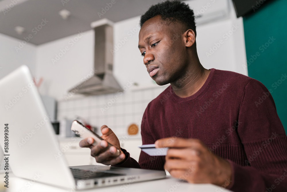 Black man shopping online in kitchen Black man shopping online in kitchen