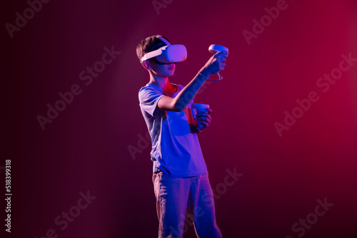 Video Gaming Concept. teenager boy playing with virtual reality goggles, VR headset, modern technology glasses with neon light on a colored background