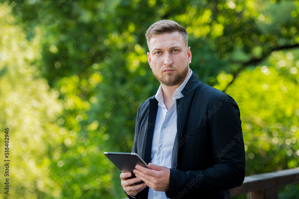 portrait of a businessman professional man with a tablet on a background of green leaves in a park garden forest portrait of a businessman professional man with a tablet on a background of green leaves in a park garden forest