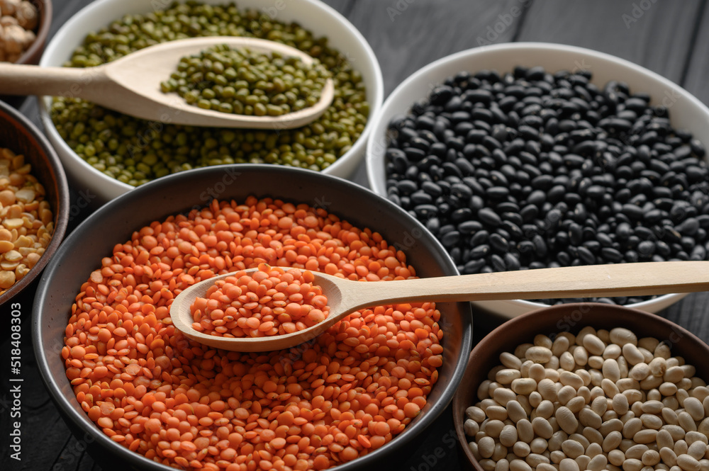 Overhead view of bowls of assorted raw legumes on a dark wooden table