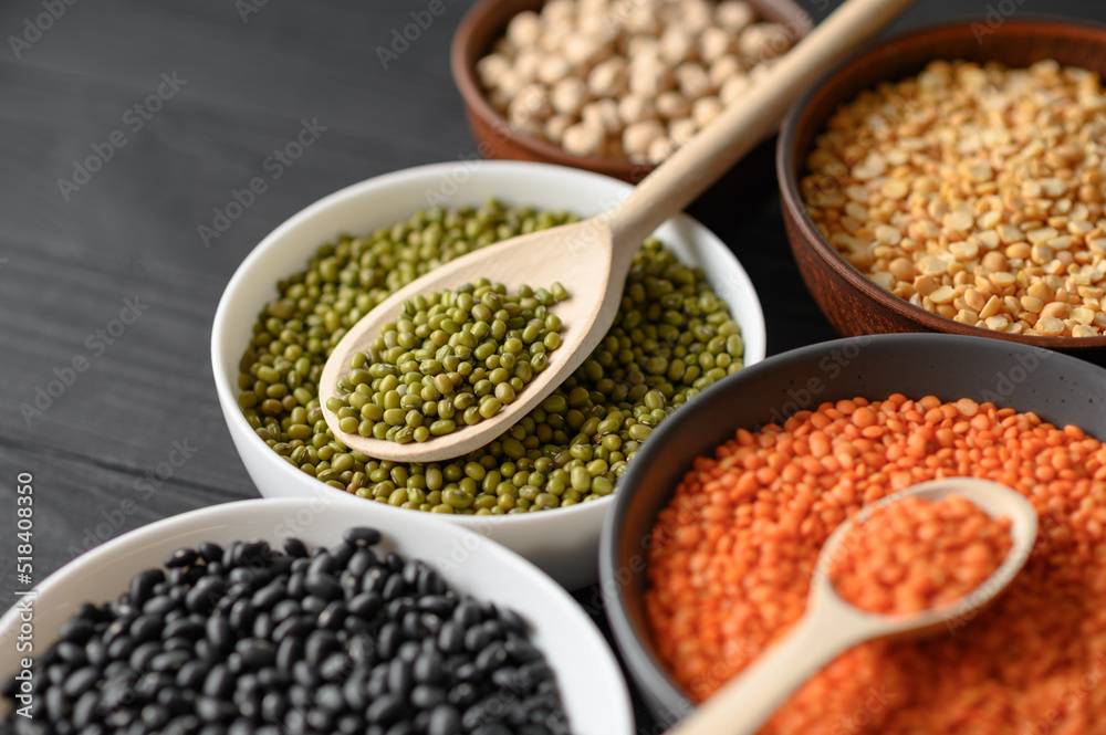 Overhead view of bowls of assorted raw legumes on a dark wooden table Overhead view of bowls of assorted raw legumes on a dark wooden table