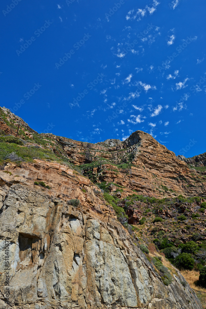 Scenic landscape of mountains against a blue sky background with scattered clouds and copy space from below. Wild plants and shrubs growing on rocky hill and cliff in a remote and natural environment