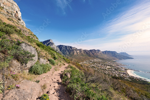 Scenic coast and rocky mountain slope with a cloudy blue sky background with copy space. A rugged landscape of plants growing on a cliff by the sea with hiking trails to explore in a rocky terrain
