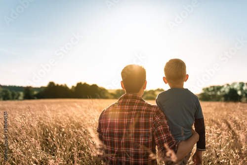 Fototapeta Father and son spending time together in nature relaxing in a field looking at the sunset, Fatherhood, and family parenting concept