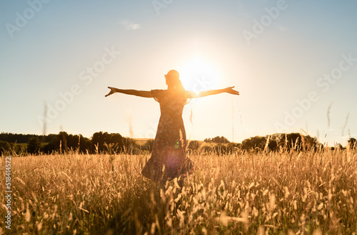 Happy woman feeling free with arms up to the sunlight in a beautiful nature sunset
