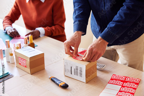 Cropped coworkers attaching fragile stickers on boxes