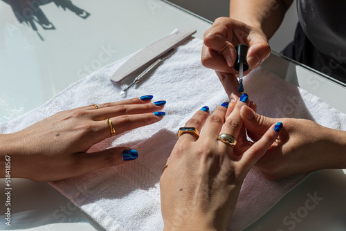Woman painting blue nails on another woman with gold rings photo