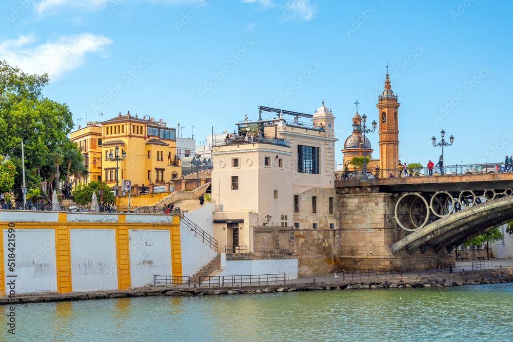 The Triana district of Seville, Spain with the Capilla del Carmen church on the left near the Puente de Isabel bridge over the Guadalquivir River.