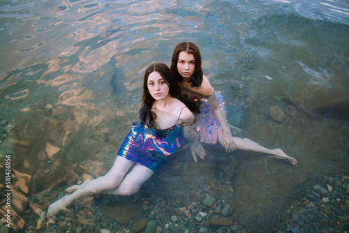 Two young women in glitter multicolored dresses in sea