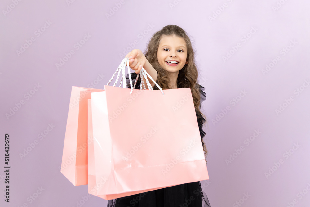 Shopping for children on Black Friday. A little girl in a black dress is very happy to shop on a pink isolated background.