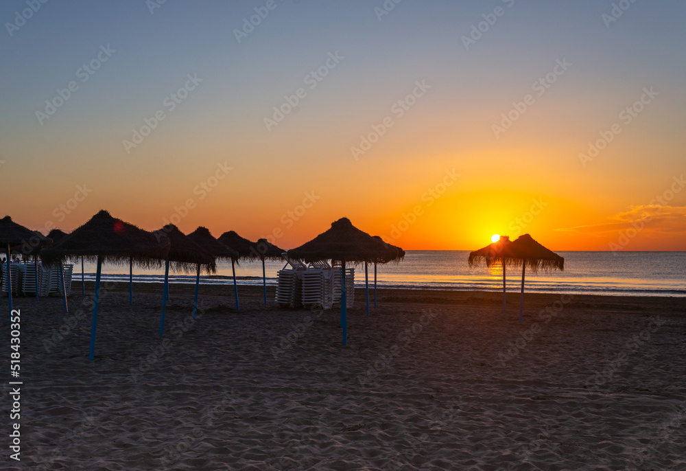 scenic seascape with reed sun umbrellas at sunrise
