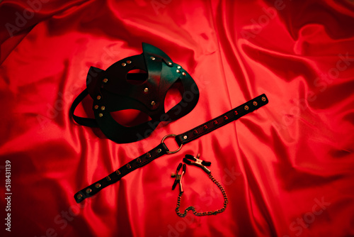 Black leather mask, necklace and nipple clamps on a red background. Love games. Love. soft focus