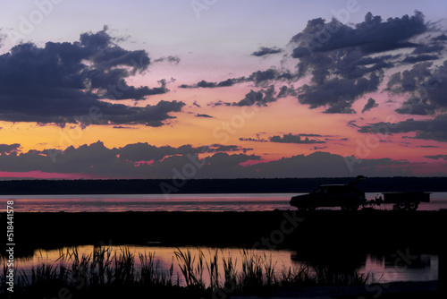 The concept of recreation on the water, the shadow of a car with a trailer on the background of water in the rays of the setting sun.
